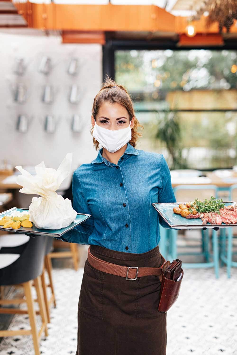 Beautiful young waitress with face protective mask working in exclusive restaurant