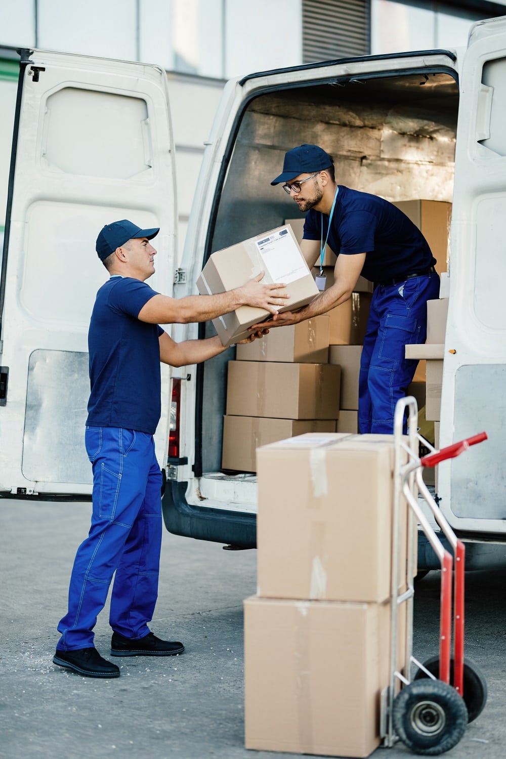 Male workers cooperating while loading cardboard boxes in a delivery van